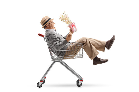 Excited mature man with a box of popcorn riding inside a shopping cart