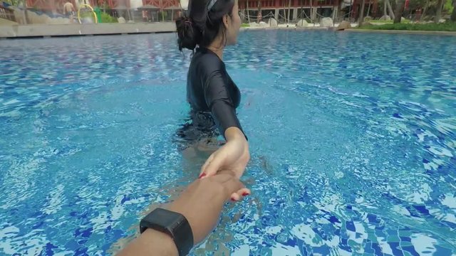 Happy young woman pulling her boyfriend hand and lead him to swim on the swimming pool