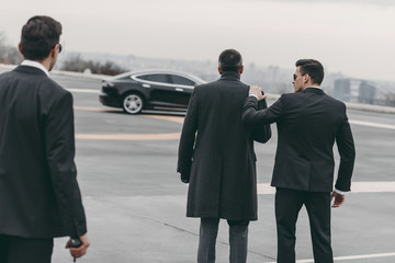 rear view of two bodyguards walking with businessman to car