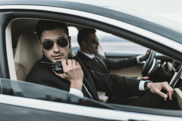 bodyguard in sunglasses talking by portable radio while sitting in car