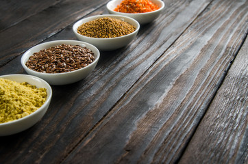 different spices in wooden spoons on a black wooden background