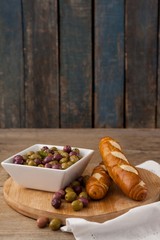 Olives in container by bread on cutting board against wall