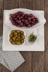 Brown and green olives by rosemary on plate