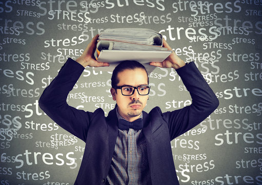 Stressed doomed business man standing with heavy folders on his head isolated on gray background