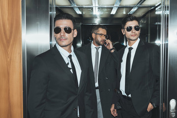 Bodyguards reviewing territory when businessman talking by smartphone in elevator