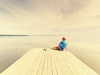 Small blond hair boy is fishing at the end of wooden mole. Smooth water level in bay