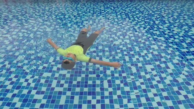 Cute little boy floating and relaxing on the pool while wearing swimsuit and swimming goggles