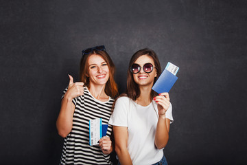 Cheerful happy girls holding passports, plane ticket and globe before grey background, indoor travel concept