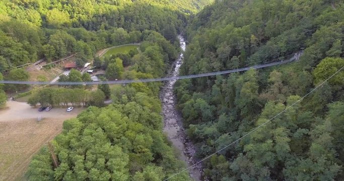 Aerial, suspended bridge in the wood with some tourist on it and a mountain river under in San Marcello Pistoiese in Tuscany, Italy