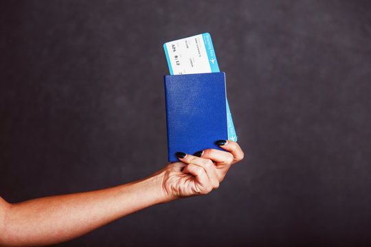Womans hand holding international passport, airplane ticket before grey isolated background