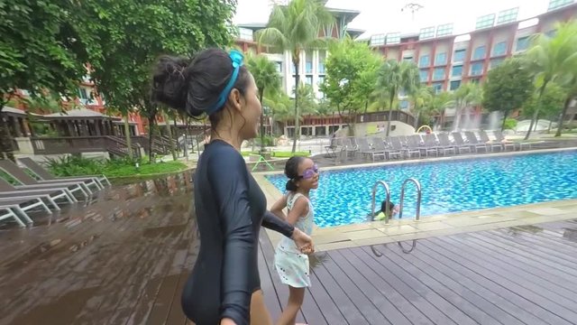 Video footage of happy little girl pulling her parent hand and leading them toward the swimming pool