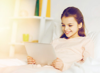 happy girl with tablet pc lying in bed at home