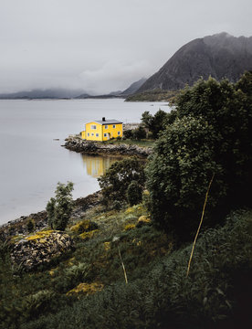 Gelbes Haus an einem Fjord in Norwegen umgeben von Wasser Bergen und mit Spiegelung