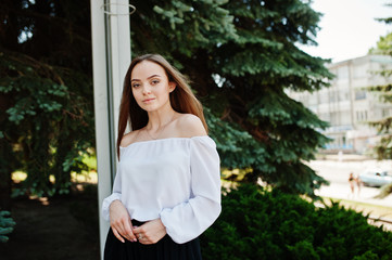 Portrait of an amazing woman in white blouse and wide black pants posing with pine trees on the background.