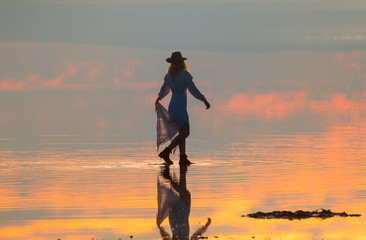 Young girl in dress and black hat walking on the salt lake beach