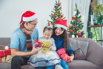 Obraz na płótnie Canvas Little asian girl and her parents open christmas gifts box on sofa at home