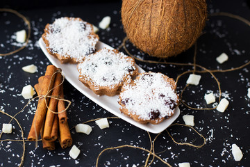 coconut muffins on a black background with cinnamon sticks and whole coconut