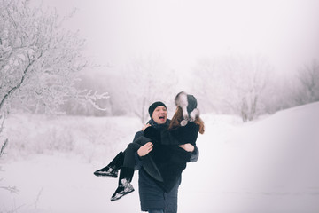 A loving couple on a winter walk. Snow love story, winter magic. Man and woman on the frosty street. The guy and the girl are resting on the snow. Christmas mood of a young family.