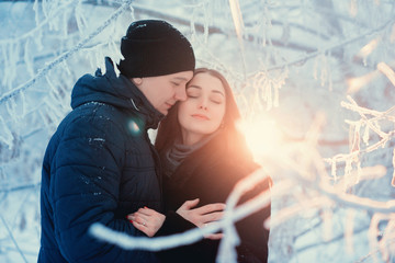 A loving couple on a winter walk. Snow love story, winter magic. Man and woman on the frosty street. The guy and the girl are resting on the snow. Christmas mood of a young family.