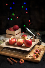 cooking of baked apples for New Year's holidays, Christmas tree and New Year's lights, honey and cinnamon on a wooden cutting board on a dark background