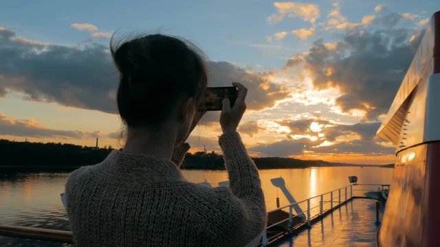 Woman silhouette taking photo of beautiful sunset with smartphone on deck of cruise ship. Sunset light, golden hour. Photography, nature and journey concept