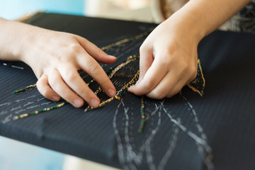 Embroidery with woman hands of flower with beads. Black fabric and Hands. Atelier or Design Studio on tailoring. Close up view.