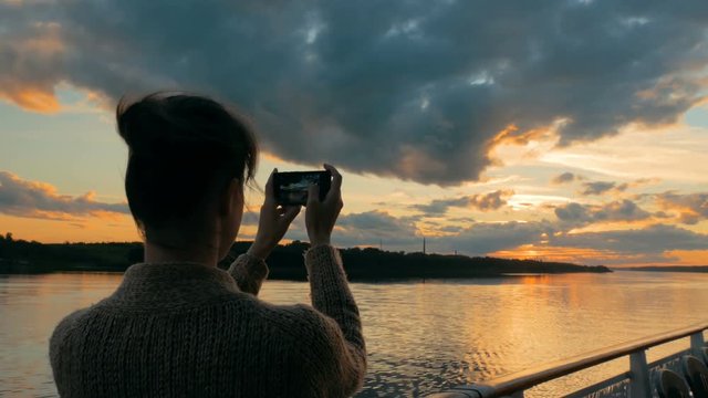 Woman silhouette taking photo of beautiful sunset with smartphone on deck of cruise ship. Sunset light, golden hour. Photography, nature and journey concept
