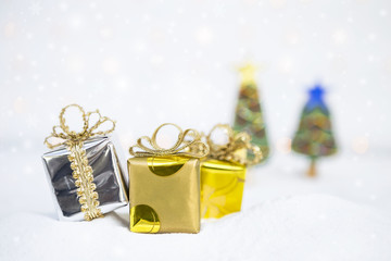 Christmas concept, beautiful gift box on white snow with blurred christmas tree and snowflake 