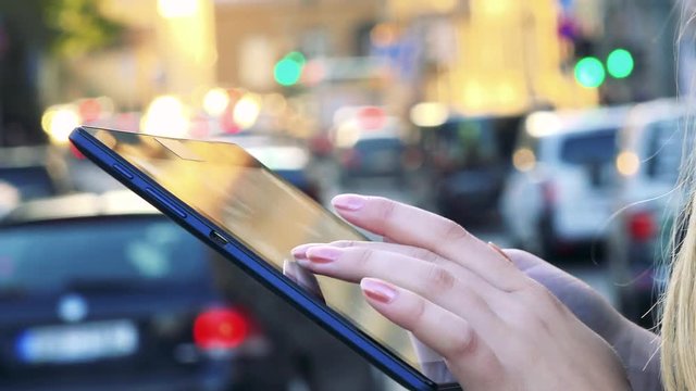 Young beautiful woman works on tablet in city - street with cars - closeup
