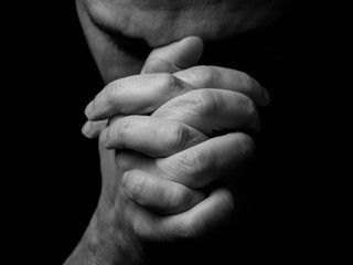 Close up of faithful mature man praying, hands folded in worship to god with head down and eyes closed in religious fervor. Black background. Concept for religion, faith, prayer and spirituality. - obrazy, fototapety, plakaty