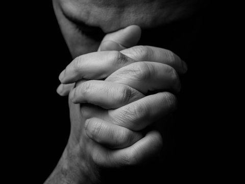 Close up of faithful mature man praying, hands folded in worship to god with head down and eyes closed in religious fervor. Black background. Concept for religion, faith, prayer and spirituality.