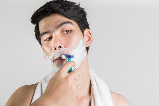 Asian handsome man is shaving looking away, white isolated - Powered by Adobe