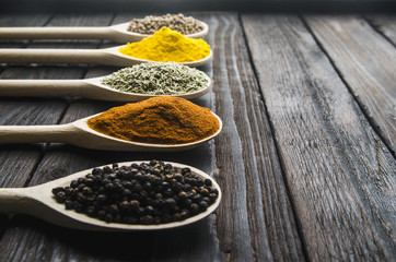different spices in wooden spoons on a black wooden background