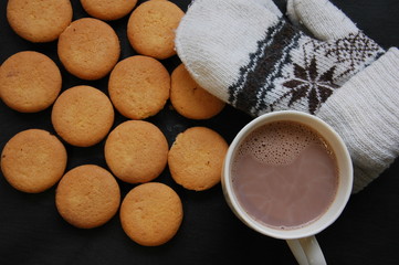 A lot of round biscuits, a cup of coffee and mittens on a black background.