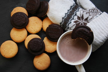 A lot of round biscuits, a cup of coffee and mittens on a black background.