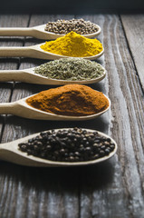 different spices in wooden spoons on a black wooden background