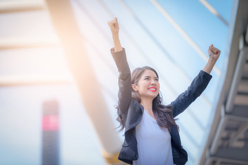 Portrait of business woman smiling with arms up celebrate on blurred city background. Business success concept