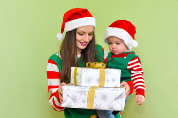 Young beautiful woman with a toddler boy in costume of Santa's helpers are holding boxes with gifts
