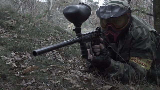 A man lying on the grass shooting from a paintball in slow motion