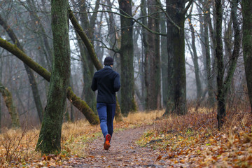 Fototapeta na wymiar Trail running in autumn park. Back view of young man jogging in fall misty forest