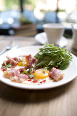 Breakfast at the table by the window. Fried eggs with bacon and herbs, hot tea in a teapot and a cup. Books, fresh flowers, bright sun from the window.