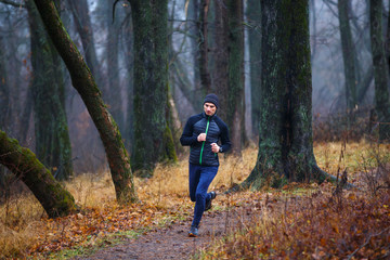 Fototapeta na wymiar Young man jogging in fall park. Trail running in cold and misty weather