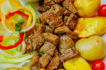 Close up of grilled meat with, potato, sweet tomatos, sald, pepper, fried plantain, served in a white plate over a wooden table, ecuadorian food