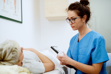 Close up of professional focused attractive nurse with eyeglasses sitting in front of woman patient with medications and clipboard at the hospital.