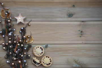 christmas food photography image with shiny gold and silver color tree branches and acorns with traditional mince pies and lit candle on a rustic natural wood background with copy space