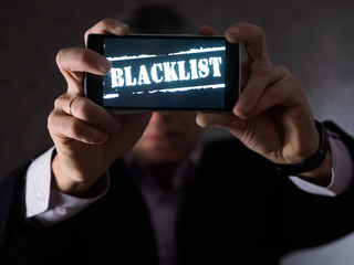 Saint Petersburg, Russia - December 5 2017. .The man is holding a smartphone in his hands, facing the viewers with the inscription Blacklist on the screen.