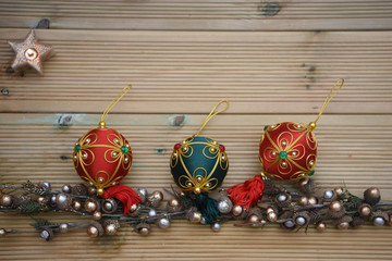 christmas photography image with red and green baubles decorations on shiny gold and silver color tree branches and acorns on a rustic wood background with copy space