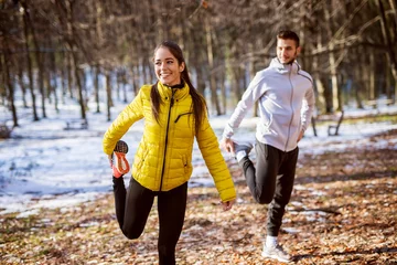 Printed kitchen splashbacks Winter sports Pretty smiling flexible girl in sportswear doing leg stretching with her personal trainer in the forest in the sunny winter morning.