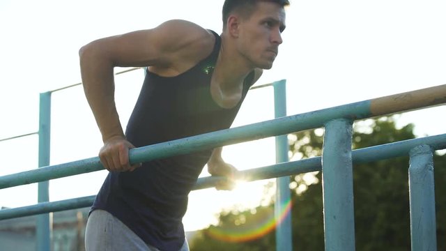 Purposeful young male doing exercises on parallel crossbars outdoors, sport