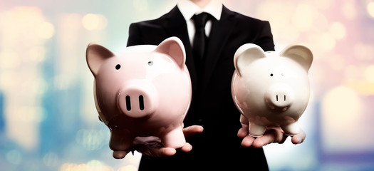 Businessman holding two piggy banks on pink and blue abstract light background